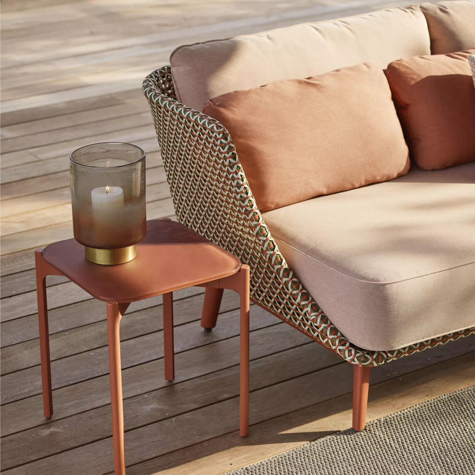 Dedon Mbarq 3er Sofa in einem Außenbereich mit Holzboden und einem Beistelltisch mit Kerze darauf