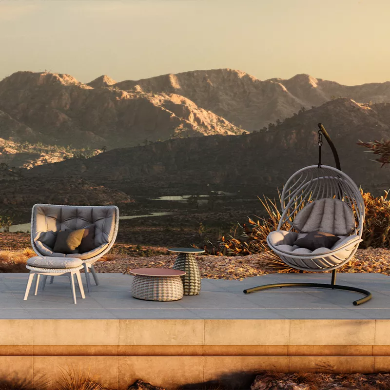 Ein Dedon Orbit Deko Kissen auf einem Hängesessel und ein Sessel mit Kissen stehen auf einer Terrasse vor einer Berglandschaft im Sonnenuntergang.