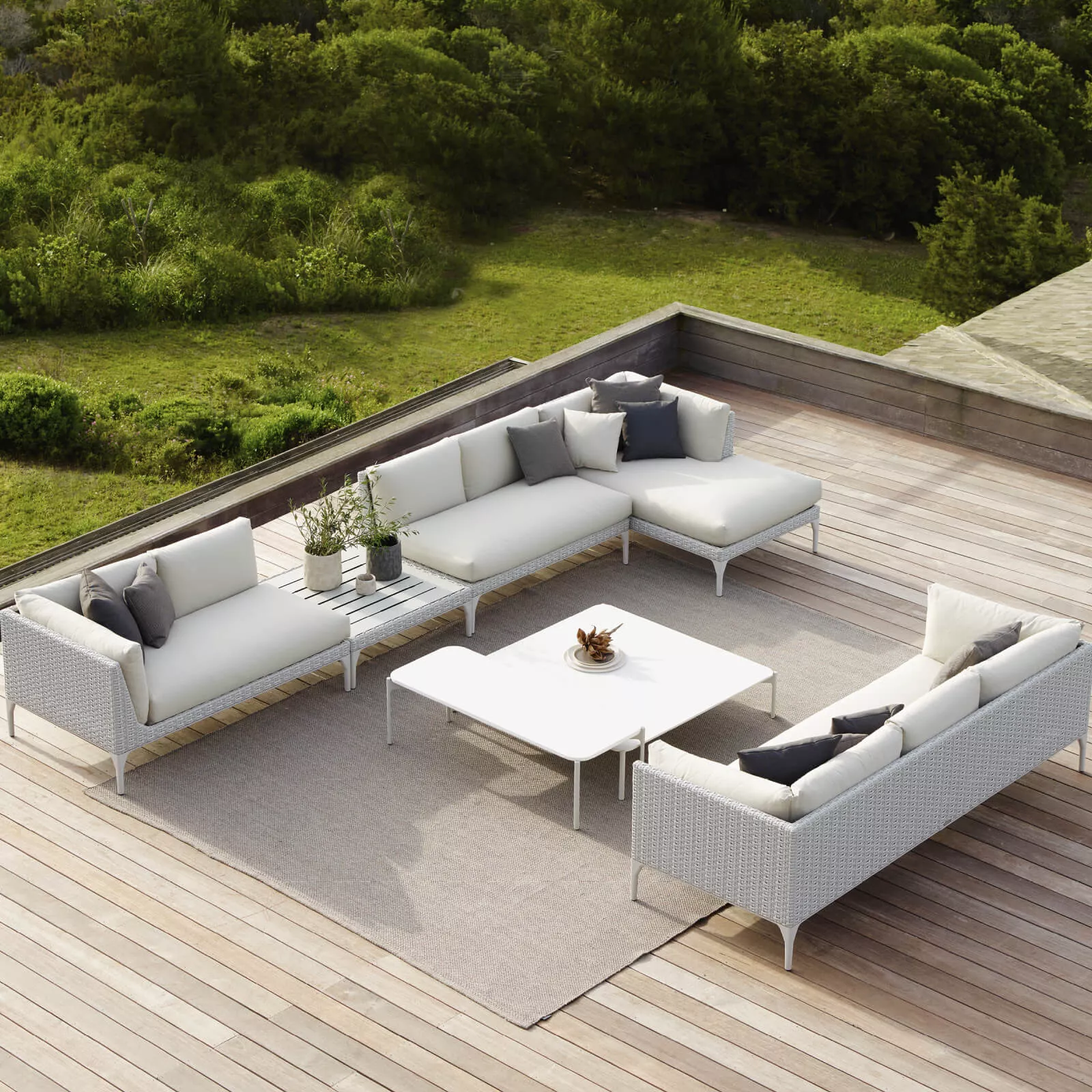 Dedon Izon Kollektion weiße Outdoor-Sofas und Tisch auf einer Holzterrasse mit grüner Landschaft im Hintergrund 