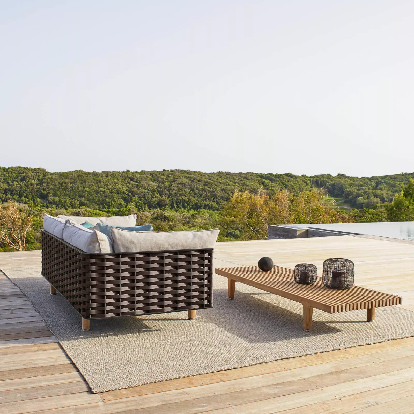 Dedon Sealine Sofa von Jean Marie Massaud auf einer Terrasse mit Blick auf bewaldete Hügel und einem niedrigen Holztisch mit Dekorationen