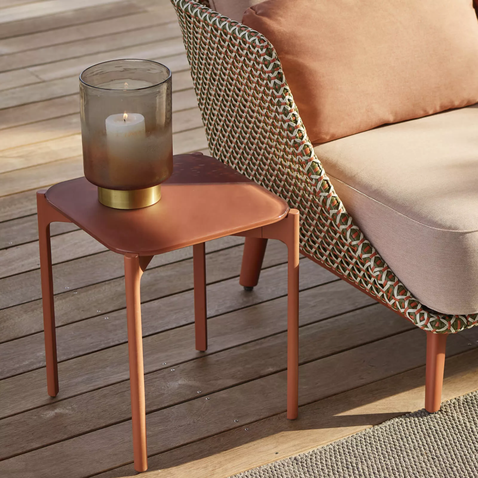 Dedon Izon Kollektion Beistelltisch in Terrakotta mit Kerze auf einer Terrasse neben einem geflochtenen Sessel 